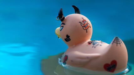 Vue de dos d'un canard en plastique à l'attitude rock n roll qui porte des tatouages et un piercing dans une piscine.