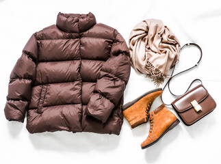 Women's brown down jacket, cashmere scarf, leather shoulder bag, oxford suede boots on a light background, top view. Autumn, winter women's clothing fashion concept © okkijan2010