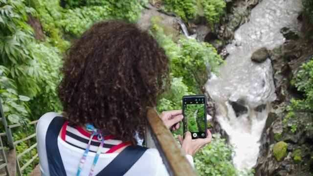 Girl taking pictures of a waterfall, stream in Bali, Indonesia. Slow motion video.