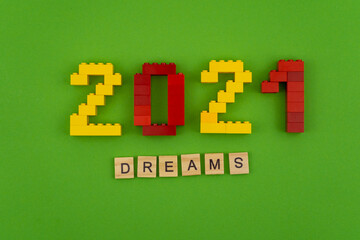 The word dreams 2021 is lined with wooden letters on a green background. Figures from the constructor top view. Postcard in place for text. Flatlay. Yellow and red numbers. Copy space.