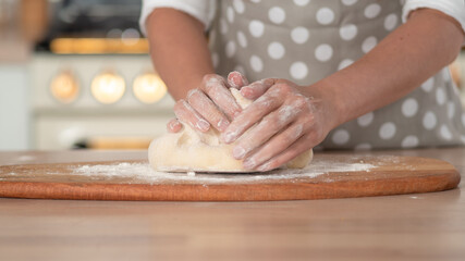 Obraz na płótnie Canvas Knead dough, hand dough and flour close-up. A pastry chef in a grey polka-dot apron.