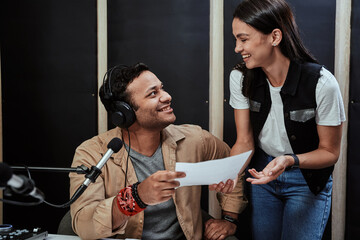 Portrait of young male radio host looking at his female colleague while receiving, holding a script...