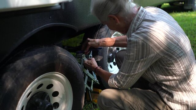 Closeup of elderly woman unscrewing a tire locking chock on an RV.