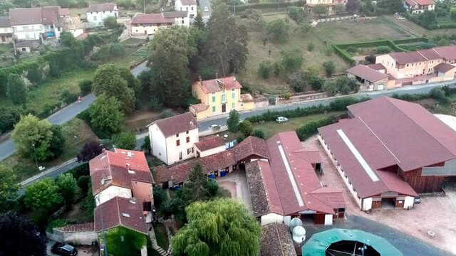 upwards moving revealing drone shot of a horse running field, with tractors moving on it. In a tower in distance and the rest of the town France, Cluny.