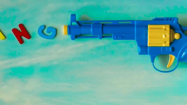 A real time rightward trucking shot of toy gun with toy letters, B A N G, placed in that order in front of the gun giving an illusion of the letters coming out of the gun with a sky background