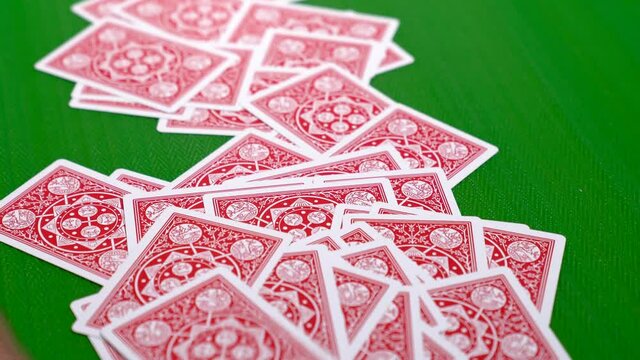 A pile of red backed playing cards being pushed into frame on a poker table in 4K