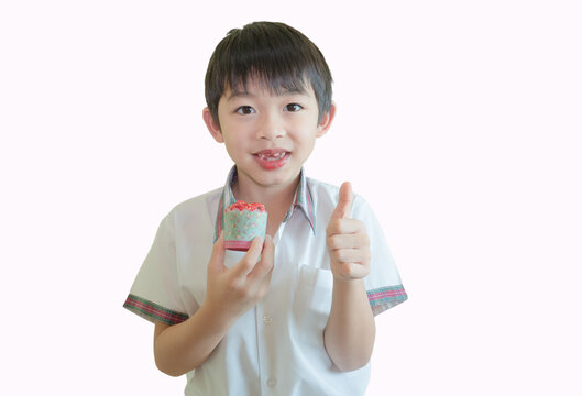 One handsome little Asian boy is holding and eating a small red butter cream cupcake isolated over white background. The happy with the favorite snack concept.
