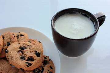 Cup of fresh milk with homemade chocolate chip cookies on white background. Healthy breakfast. Selective focus
