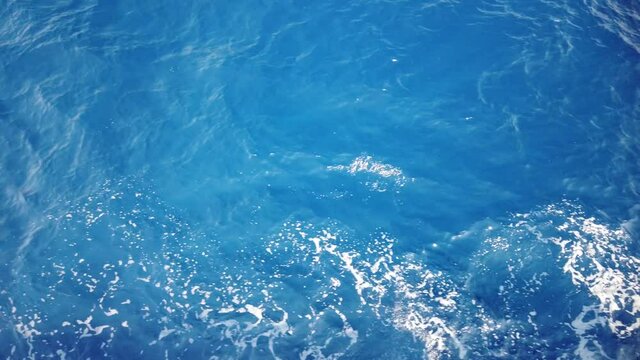 Water trail on blue sea surface from floating ship close up. Trail turquoise sea water with foam and waves, spills, bubbles, traces from ship.
