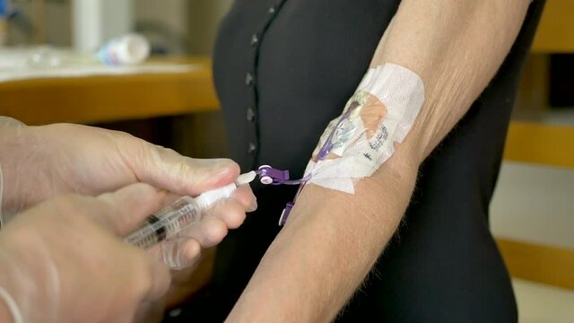 Medical nurse doing an at home iv patient visit wearing sterile gloves while finishing a saline solution injection  from a syringe into a picc line and capping it off.