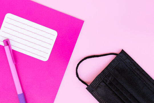 Notebook, pen, black medical mask on a pink background. Concept.