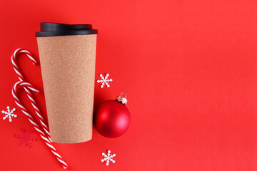 A cork coffee Cup, snowflakes, lollipops and a red Christmas ball on a red background. Christmas composition. A festive concept for a coffee shop. The view from the top. Flatly. Copyspace.