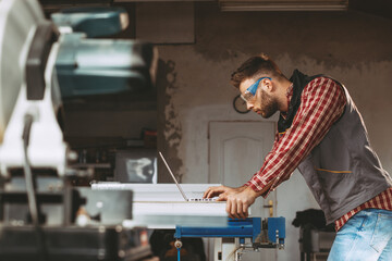 Young man work in home workshop using laptop and reads the manual