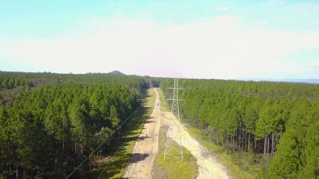 Aerial tracking drone shot rising close to powerlines, following a off-road motorcycle rider, racing on a sand dirt bike track, at Glass house mountains national park, in Queensland, Australia
