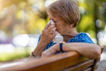 Unhappy senior woman wipes her eyes with a tissue outdoors
 - Powered by Adobe