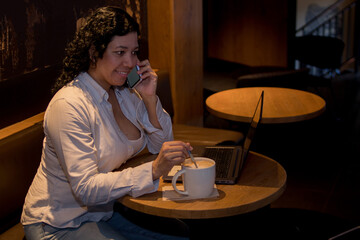 Caucasian woman in a coffee shop working with a laptop while talking on the phone and had a coffee