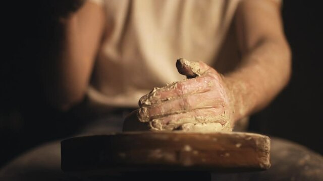 A man shaping clay with his hands on a mill in slow motion.