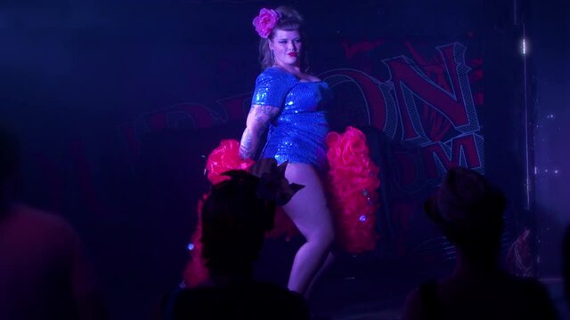 Curvy burlesque dancer shakes her hips on stage with a red feather boa during a sexy live performance