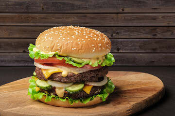 Hamburger on dark rustic wooden background. Tasty homemade gourmet burger or cheeseburger with two patty or cutlets and lettuce.