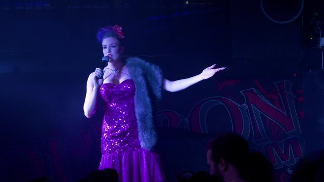 Female performer on stage rants to the audience while pacing back and forth on stage