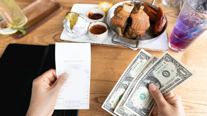 Selective focus of woman hand as receipt bill  food and drink for payment by  cash of dollar  in the restaurant