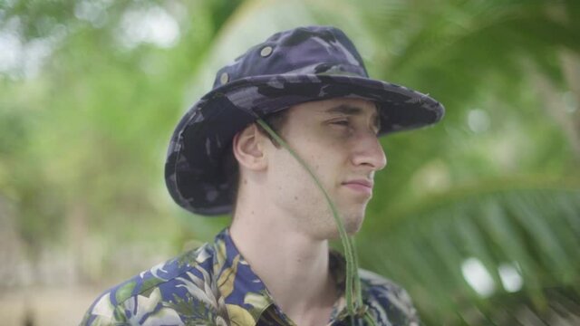 Young Man in park ranger explorer outfit and wide brim hat stares into the distance in tropical Jungle
