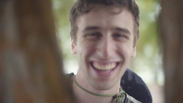 Smiling young man plays peek-a-boo with camera through tree branches