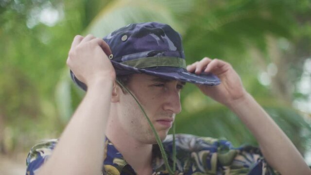 attractive white Male in Explorer costume puts on his Camouflage hat while scanning and exploring Tropical Jungle