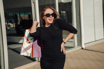 Portrait of european lady hold hand colorful bags woman after shopping in black dress sunglasses on head retail store near mall on the street sunshine sales black friday season bokeh background