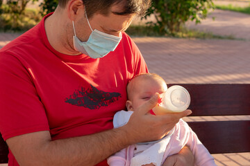 Primer plano de un padre sentado en un banco de un parque. El padre que lleva una mascarilla...