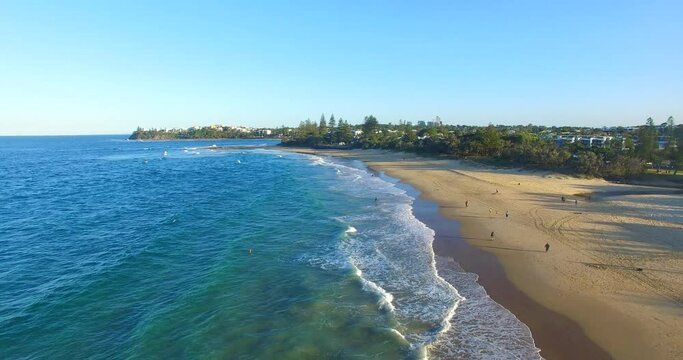 Reverse drone shot of the coastline at Dicky Beach showing waves and the beach expanse.