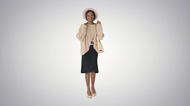 Stylish african american woman in knitwear and white hat dancing while walking on gradient background.