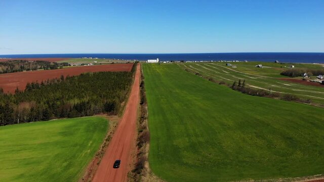 Black car driving along a red dirt country road towards the ocean
