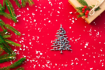 Christmas tree of screws, gift with branches of a Christmas tree and berries on a red background. Flat lay. Copy space.