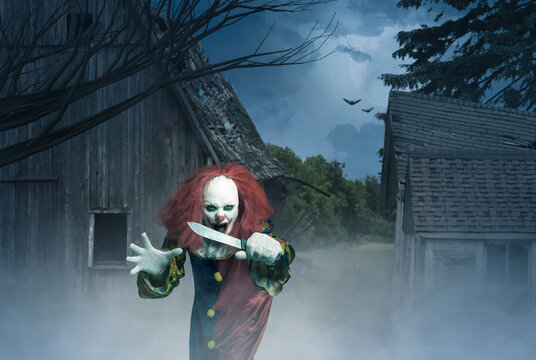 crazy clown with a knife in the hand in front of a scary scene