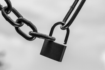 Backlit monochrome padlock and steel chains close up  symbolizing lockdown