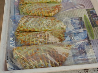 A Thai coconut waffle, so called ' Kanom Rung Peung ' or literally ' bee hive snack ', being put in a clear plastic bag being ready to be sold and eaten - street food in Thailand