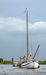 Naklejka premium Wooden sailing boat with lowered sails awaits an approaching rainstorm. In the background a traditional Dutch windmill.