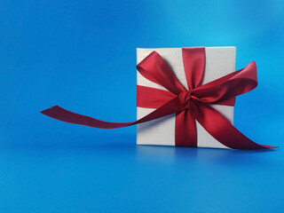The red ribbon present or gift box in blue background. Christmas or birthday present and thanksgiving, more give the more receive concept. people showing love in valentines day.