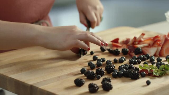 Woman slicing blackberries on a wood cutting board with people in the background