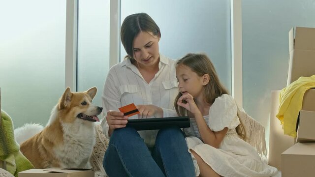 Mother With Her Daughter Spending Money Together.The Mother, a Child and Their Dog Uses a Credit Card for Online Shopping.Purchase Confirmation by the Internet.Uses a Tablet For Online Shopping.