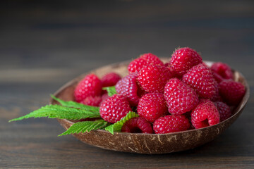 Harvest of ripe farm raspberries in coconut plate on the wooden table background. Close up