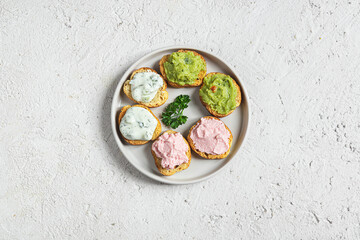 Variety of small sandwiches on the gray plate. Appetizing crostini with tarama, tzatziki and guacamole sauce.