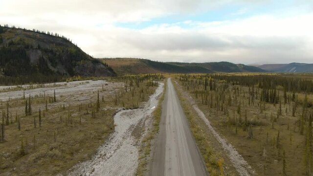 View of Scenic Road from Above surrounded by Mountains and Forest on a Cloudy Fall Day. Aerial Drone Shot. Taken near the Dempster Highway, Yukon, Canada.