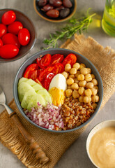 Healthy salad bowl with buckwheat, tomatoes, boiled egg, onion ,cucumber, chickpeas and mixed greens on a table. Top view. Food and health.
