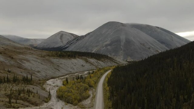 View of Scenic Road from Above surrounded by Mountains and Forest on a Cloudy Fall Day. Aerial Drone Shot. Taken near the Dempster Highway, Yukon, Canada.