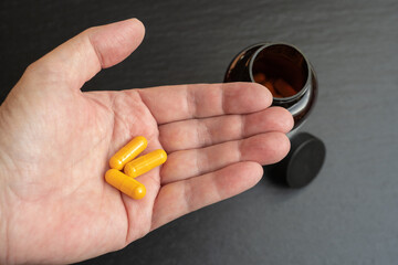 Hand with three yellow tablets capsules