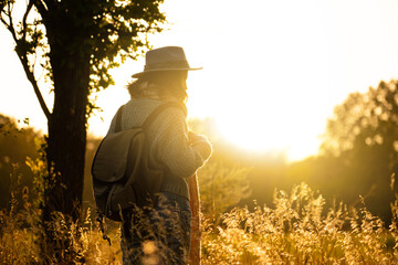 Silhouette of a woman wearing a hat and with a backpack at sunset.