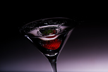martini glass and splash from strawberries on dark background