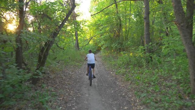 A happy child rides a bicycle in a park in the open air. Cycling on a path in the woods. Active rest of the child. Healthy lifestyle, children's sports.